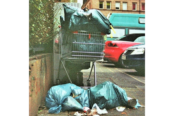 Image A shopping cart filled with trash on top of a pile of trash bags.